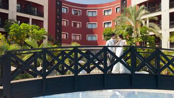 Un hotel con fachada roja curva, balcones y un área de piscina con palmeras.