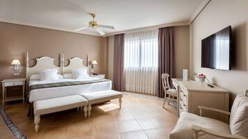 Habitación de hotel con cama, mesitas de noche, escritorio, silla, televisor y ventilador de techo.