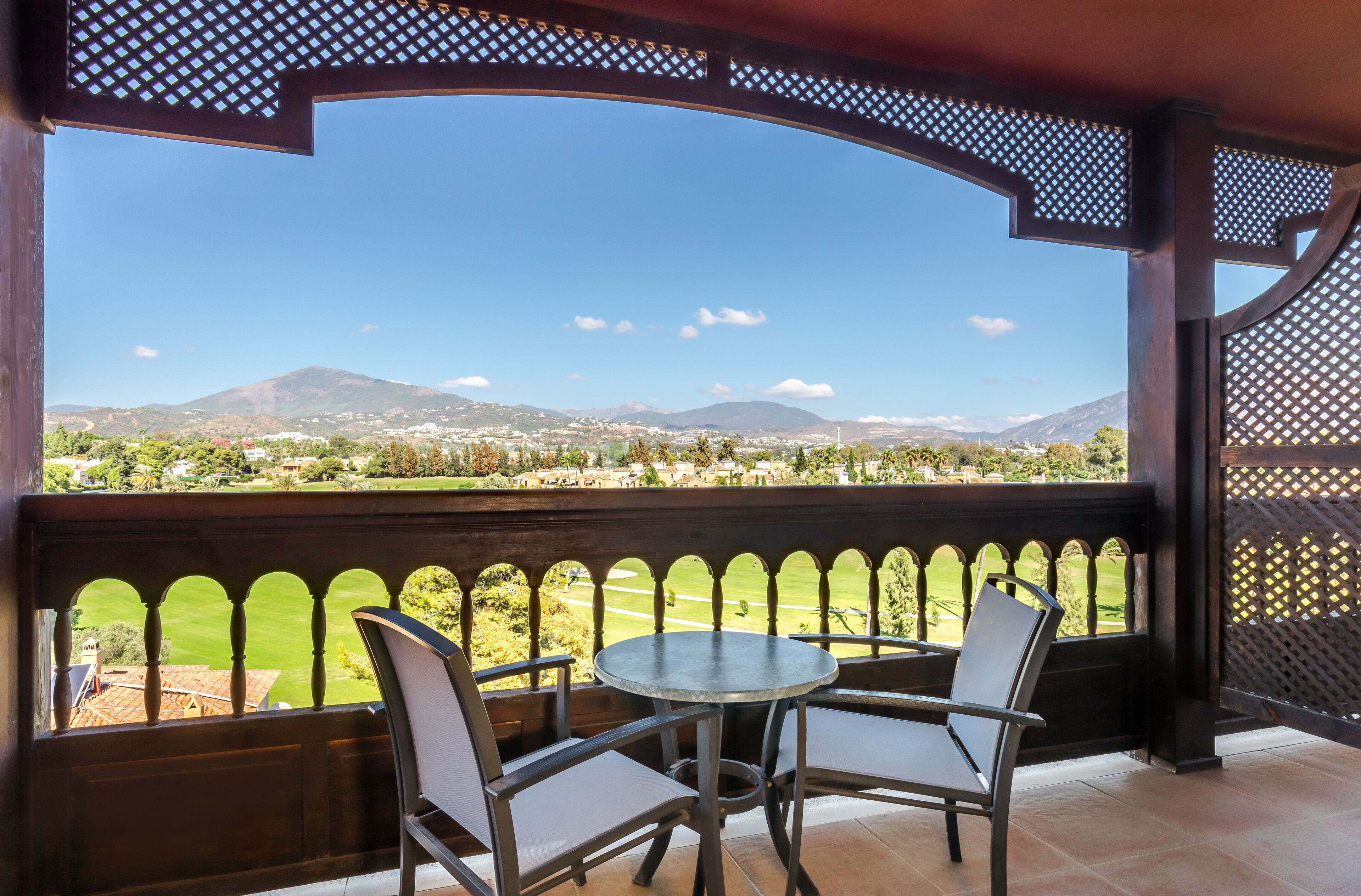 Ein Balkon mit Tisch und Stühlen, der auf eine grüne Landschaft mit Bergen im Hintergrund blickt.