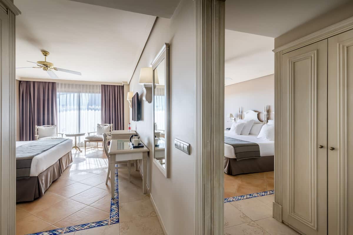 Habitación de hotel con dos camas, un escritorio, una silla, un espejo, un ventilador de techo y un armario.