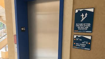 Un ascensor con estructura azul, un cartel de seguridad contra incendios y un indicador de habitaciones que muestra del 101 al 108.