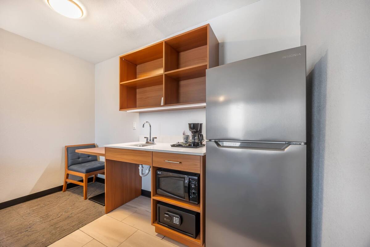 A compact kitchen with a built-in microwave, a coffee maker, and a stainless steel refrigerator.