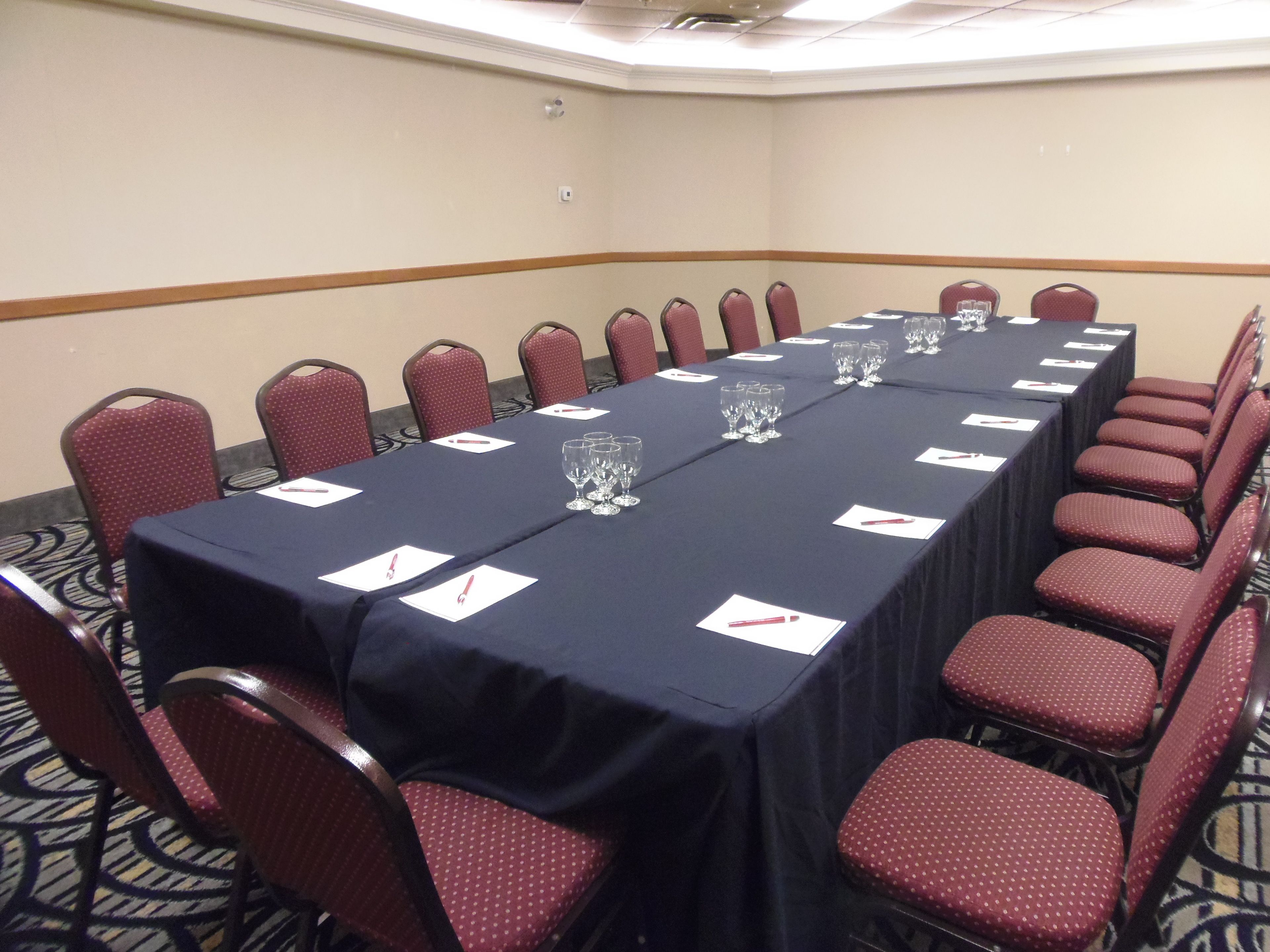 Un salón de conferencias con una larga mesa, sillas rojas y piso alfombrado.
