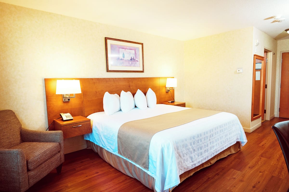 Habitación de hotel con cama, lámparas de noche, una silla, mesita de noche y un cuadro en la pared.