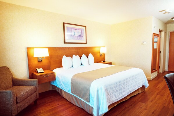 Quarto de hotel com cama, abajures, uma cadeira, mesa de cabeceira e um quadro na parede.