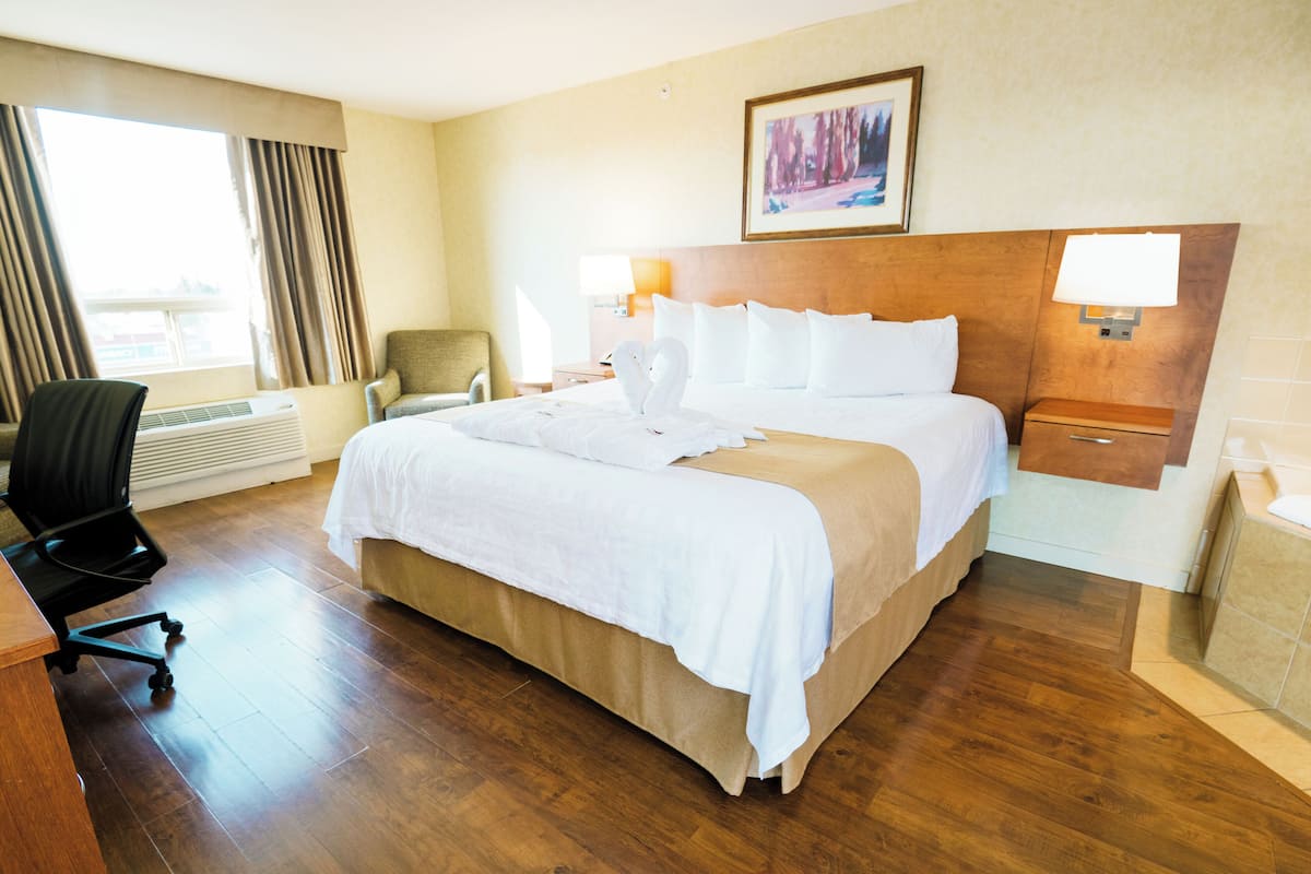 Una habitación de hotel con una cama grande, un escritorio, una silla, una lámpara y un cuadro en la pared.