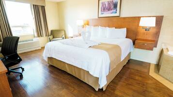 A hotel room with a large bed, a desk, a chair, a lamp, and a painting on the wall.