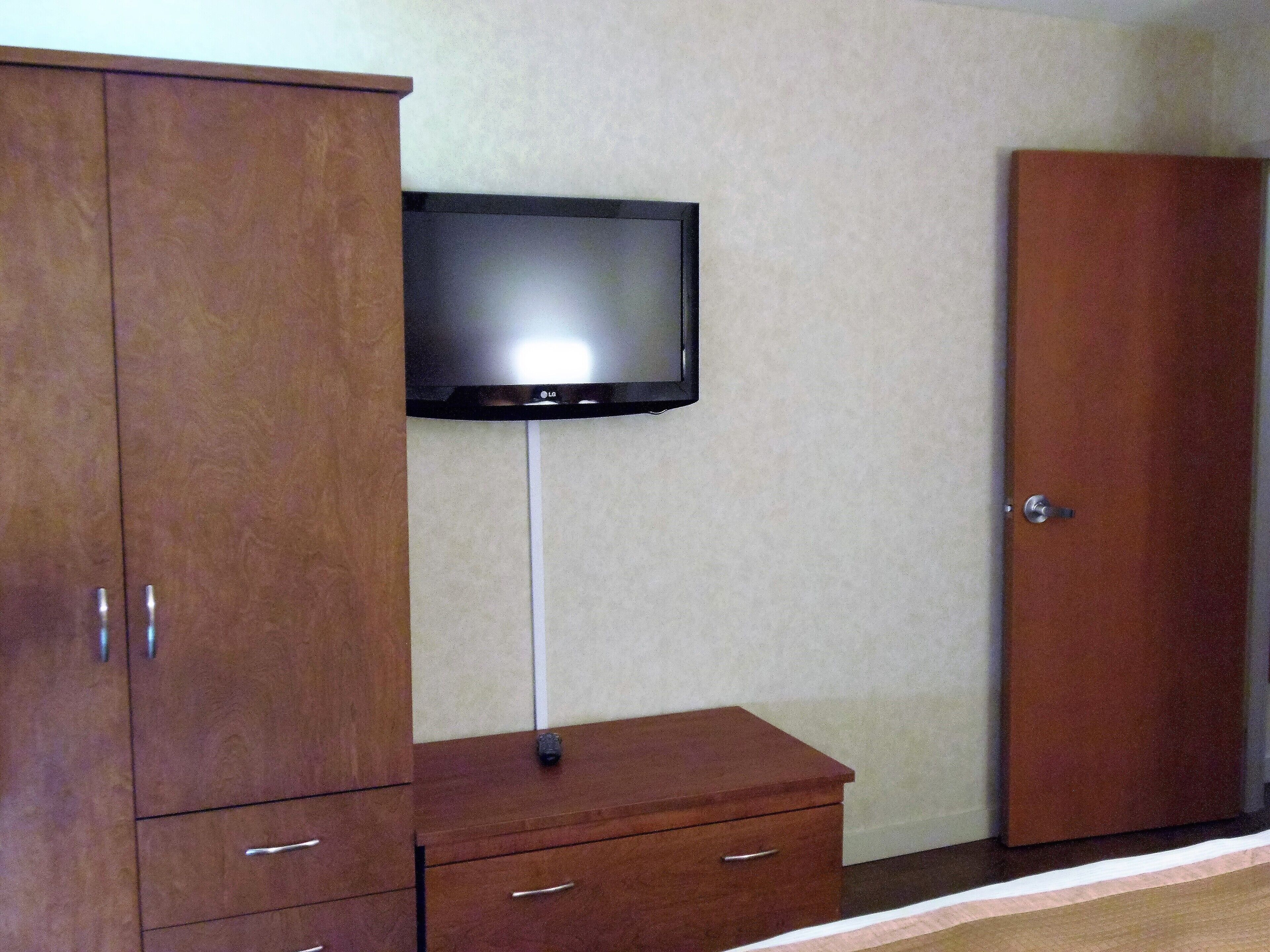 Une pièce comprenant une armoire en bois, un petit meuble en bois et un téléviseur fixé au mur.
