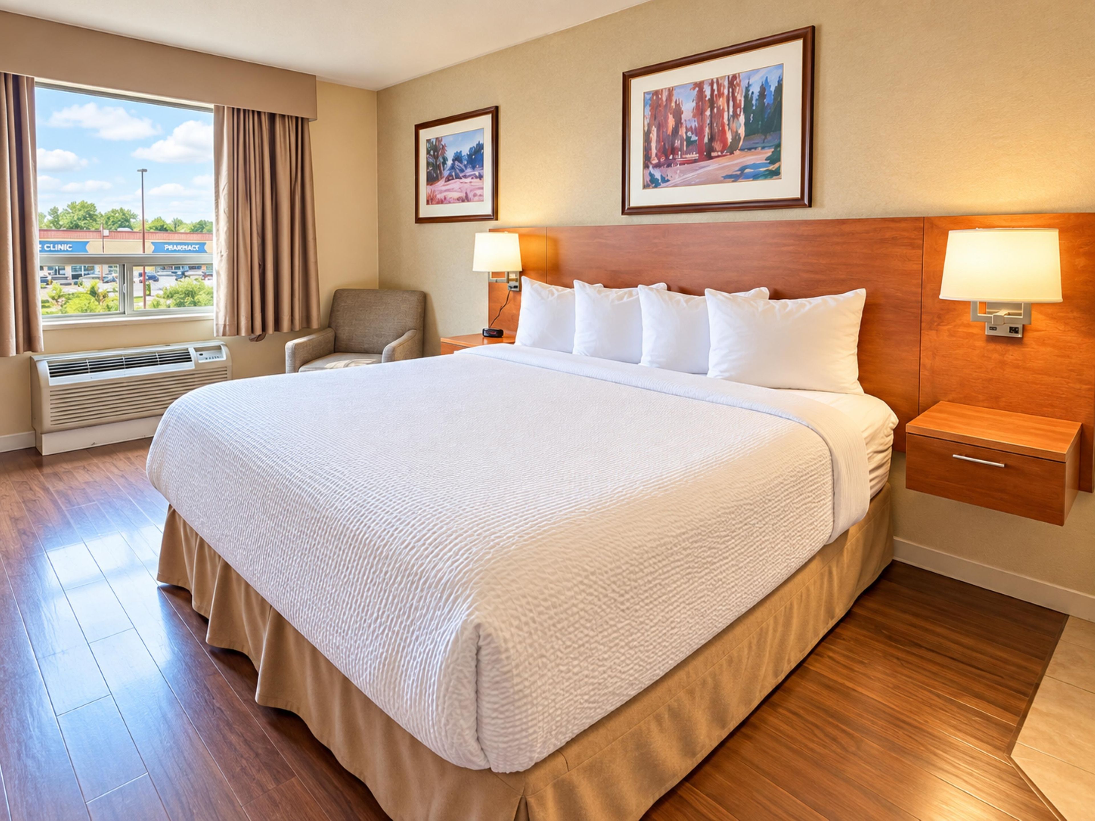 A hotel room with a large bed, two bedside lamps, a chair, a window with curtains, and two framed pictures on the wall.