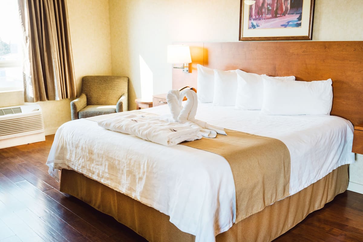 Una habitación de hotel con una cama grande, una silla, una lámpara y un cuadro en la pared.