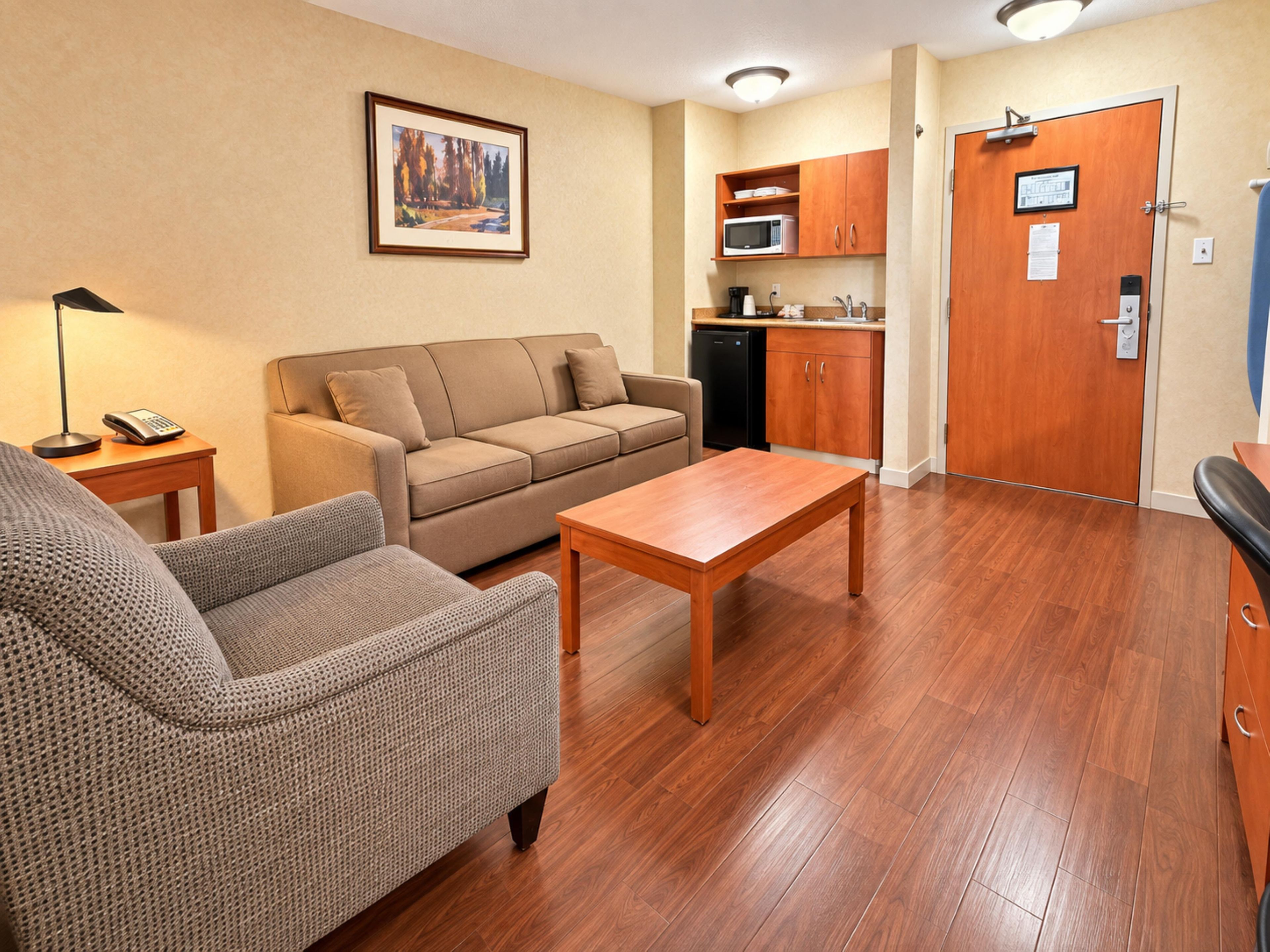 Una sala de estar amoblada con sofá, sillón y mesa de centro, una kitchenette con microondas, y una puerta con cerradura.