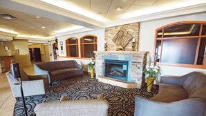 A hotel lobby with a fireplace, sofas, a patterned rug, and a stone accent wall. - Rosslyn Inn and Suites (Edmonton)