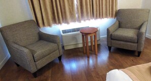 Um quarto com duas poltronas, uma pequena mesa de madeira e um aquecedor portátil.