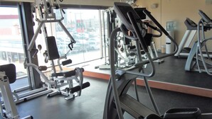 A gym with various exercise machines, a large mirror, and a view of parked cars outside. - Rosslyn Inn and Suites (Edmonton)