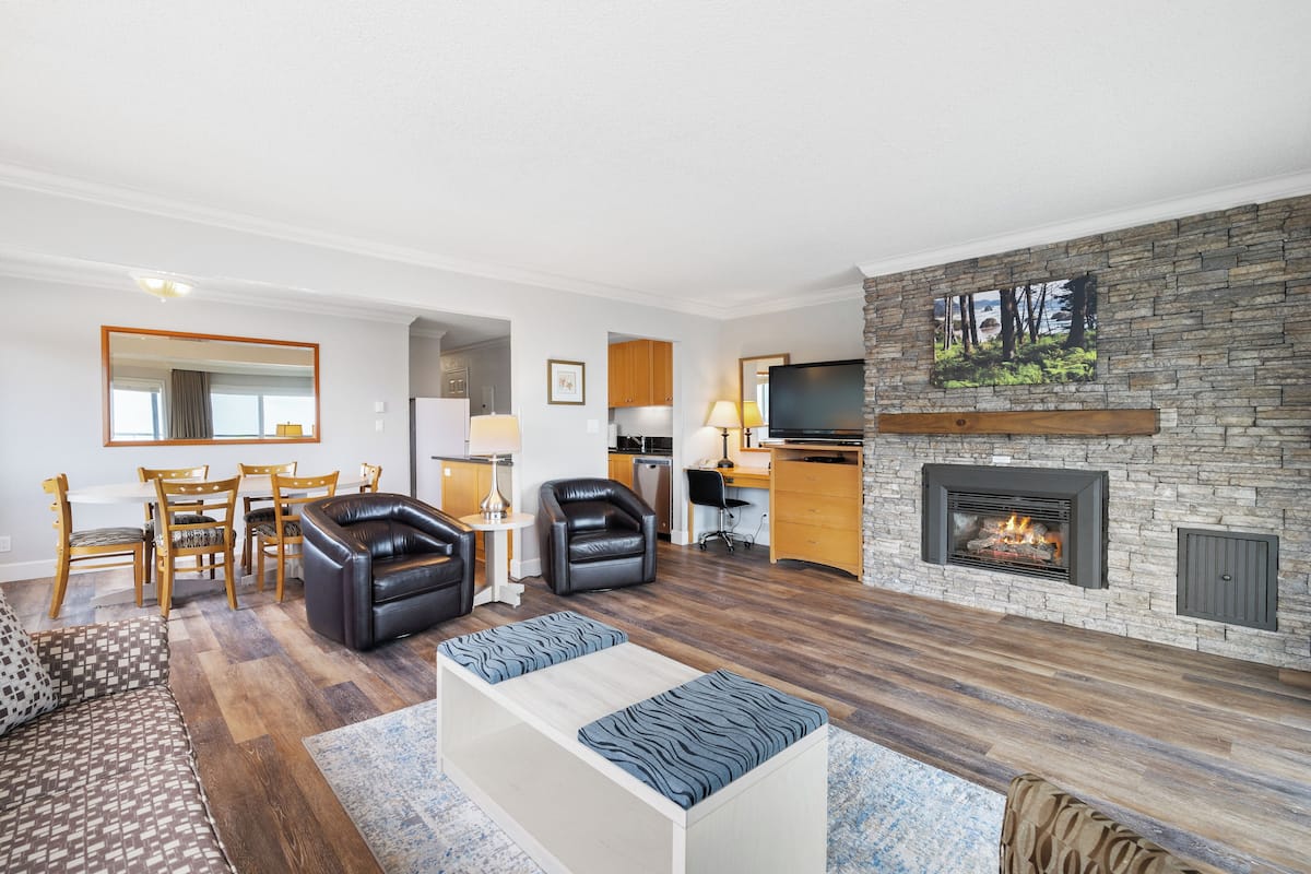 A modern living room with a fireplace, a dining area, and a kitchen.