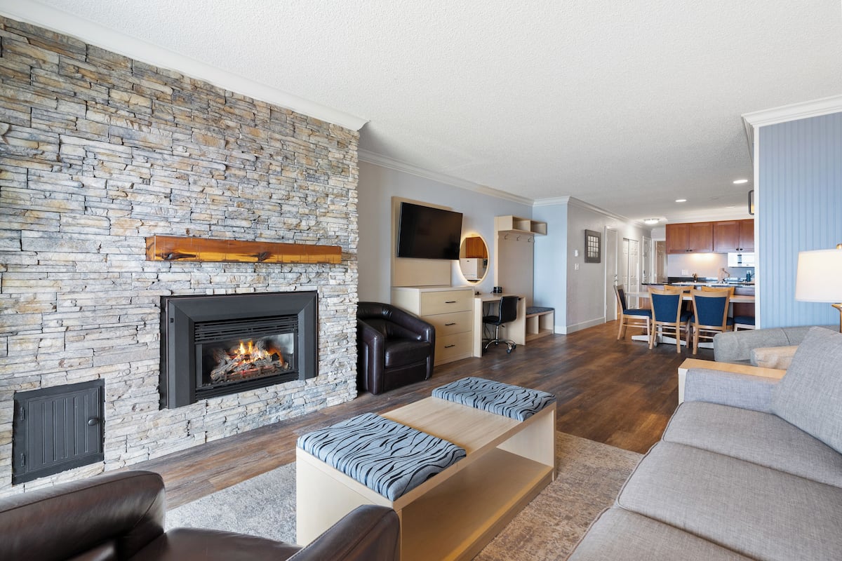 A modern living room with a stone fireplace, a sofa, a coffee table, and a dining area in the background.