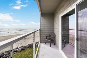 Uma varanda com vista para a praia, uma cadeira e uma porta que dá para outro quarto.