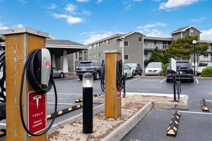 Un estacionamiento con estaciones de carga para Tesla, un área cubierta y un edificio al fondo.