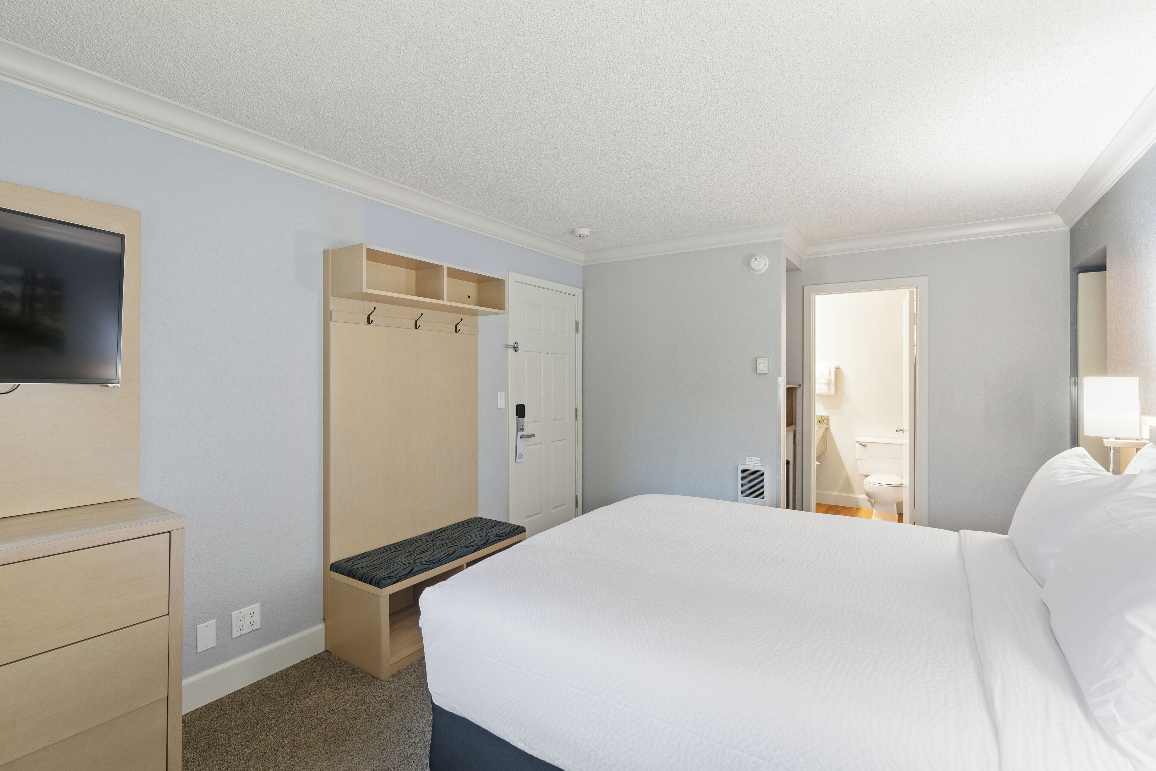 Una habitación de hotel con cama, televisión, armario y un banco.