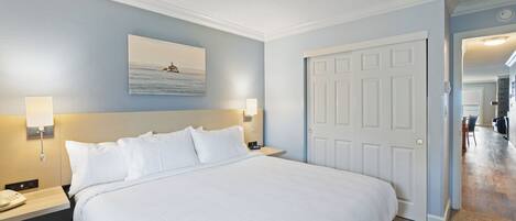 Une chambre d’hôtel avec un grand lit, une table de chevet avec un téléphone, une lampe fixée au mur et une porte donnant sur une autre pièce.