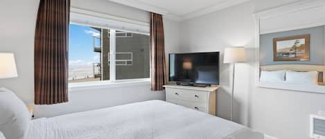 A hotel room with a large bed, a television, a dresser, and a window with curtains.