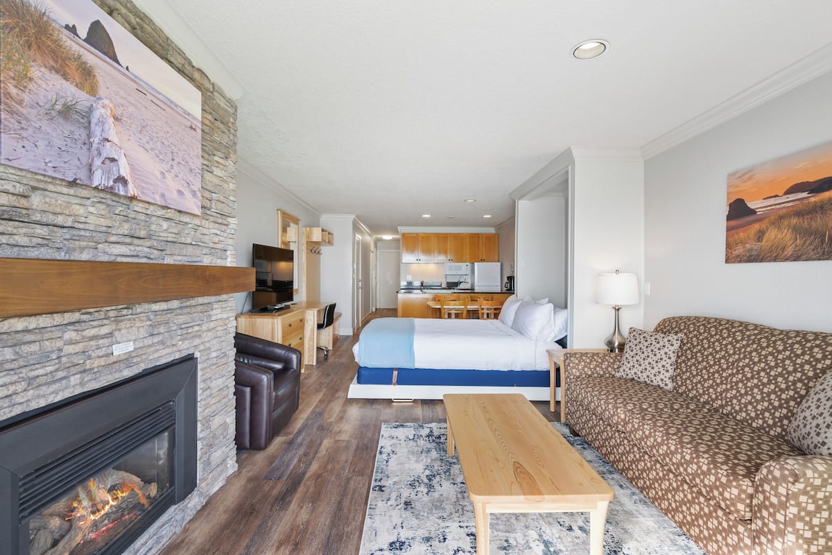A modern living room with a stone fireplace, a sofa, a coffee table, and a bed with a blue accent.