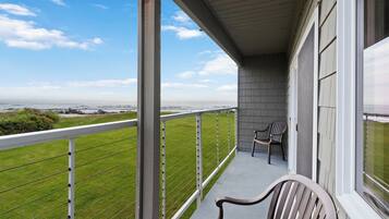 A balcony with a view of the ocean, a chair, and a table.