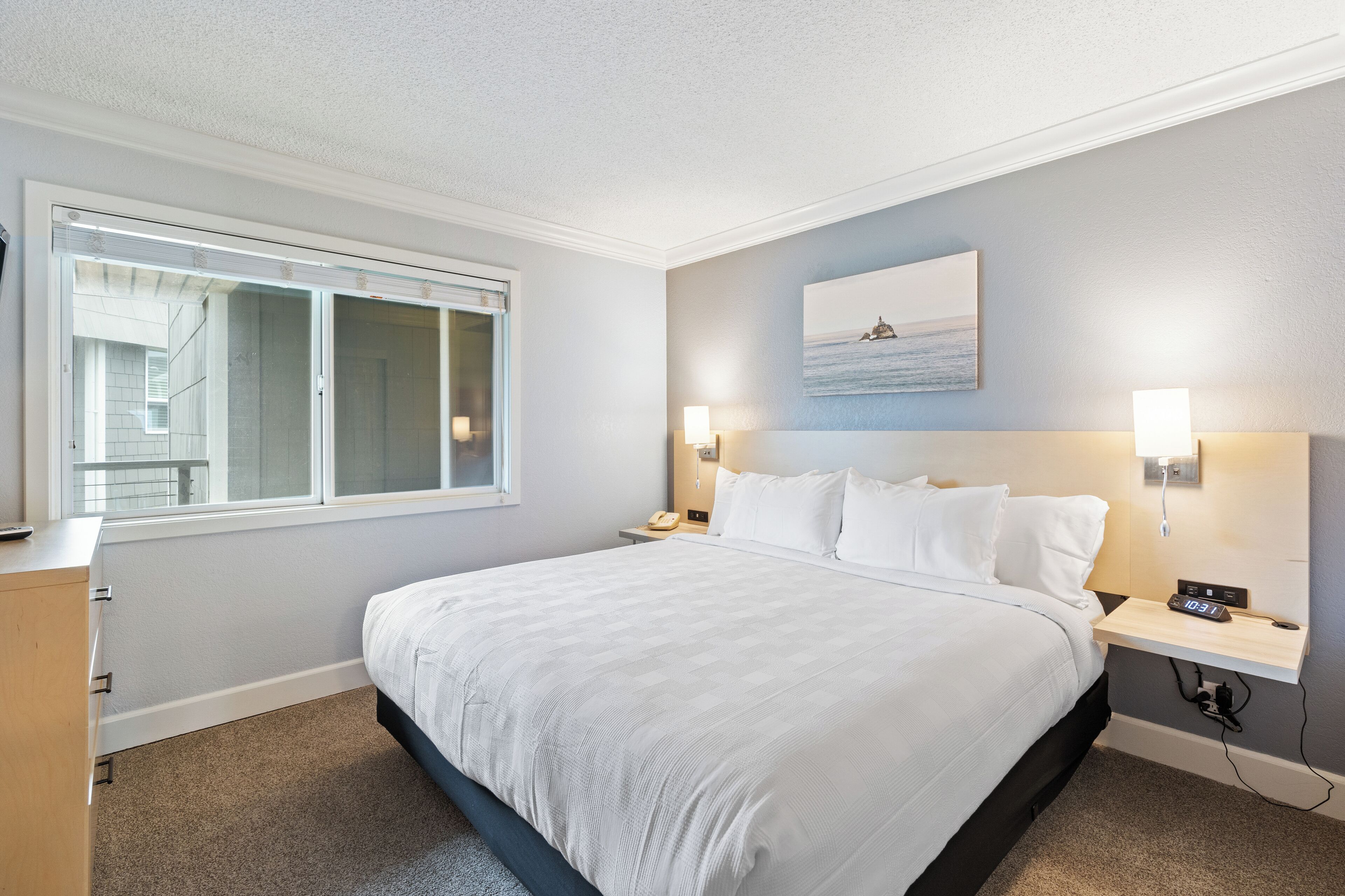 A neatly arranged hotel room with a large bed, bedside lamps, a nightstand, and a window with blinds.