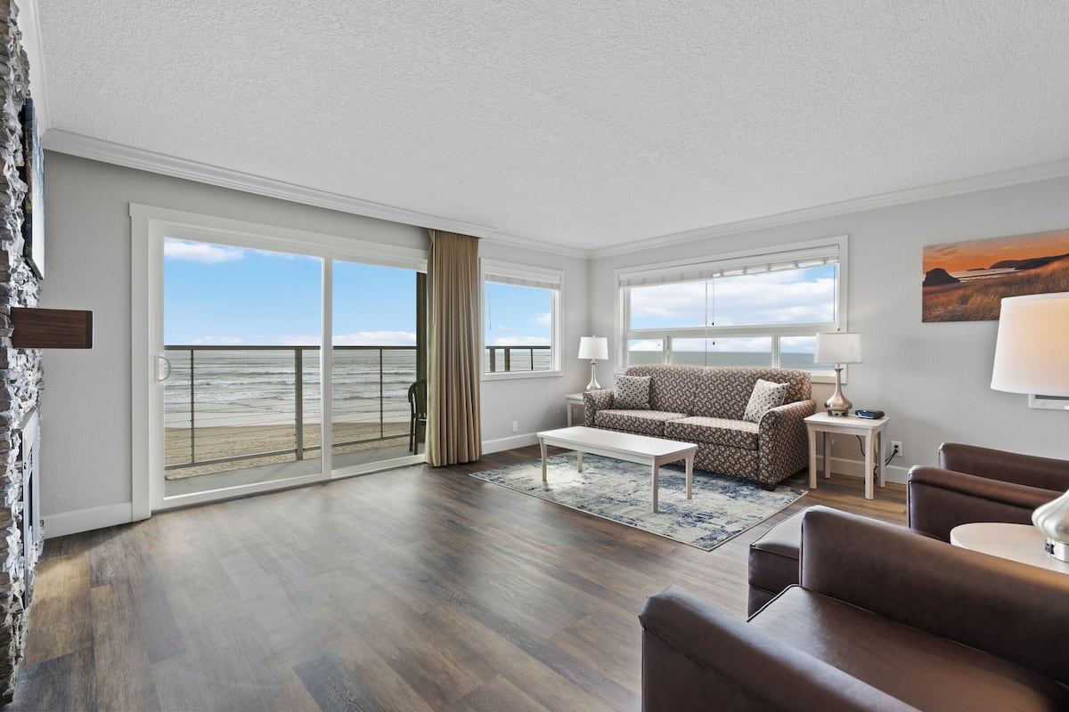 A spacious living room with a large sliding glass door leading to a balcony, a sofa, a coffee table, and a lamp.