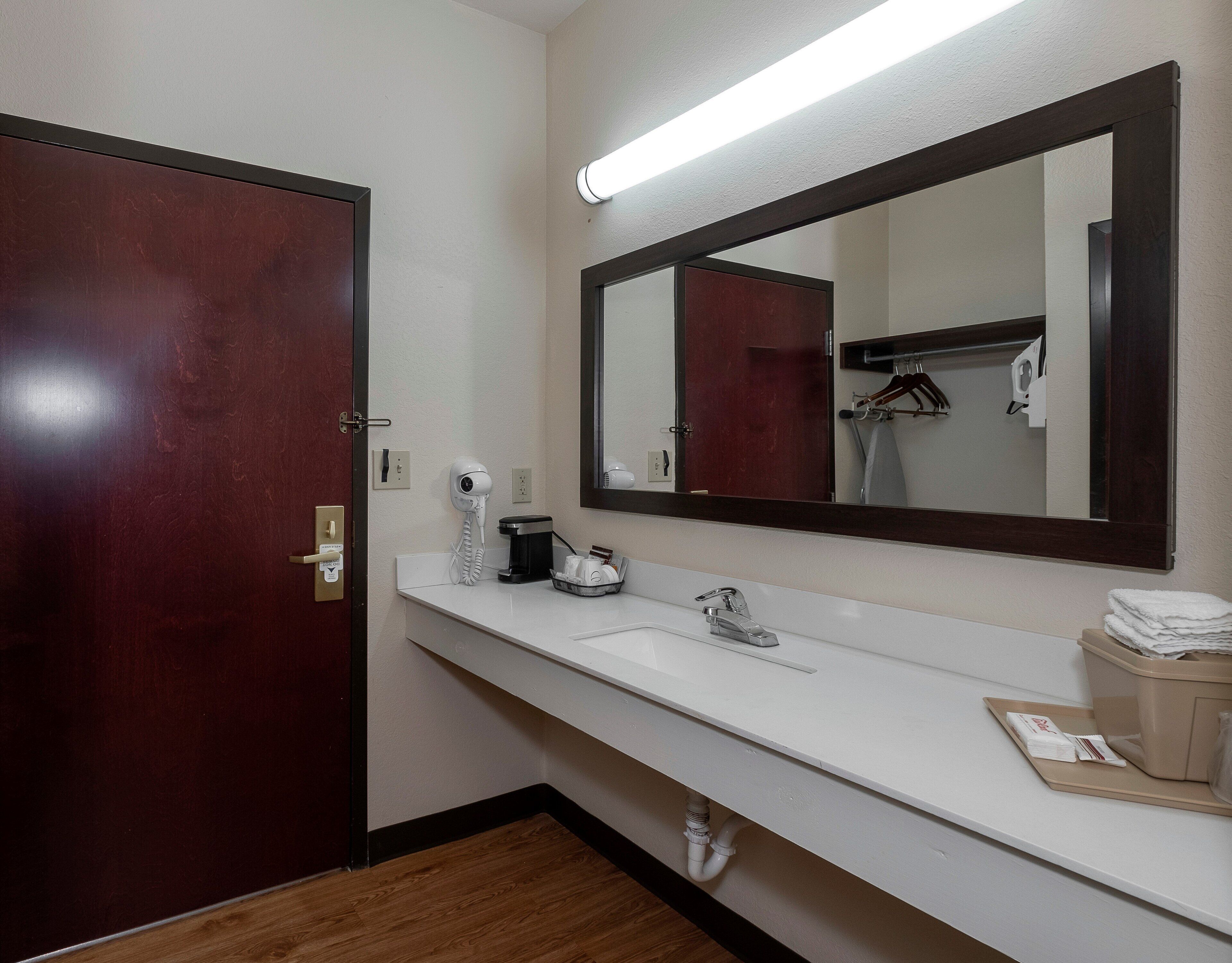 A hotel bathroom with a wooden door, a white sink with a mirror above it, and a towel dispenser.