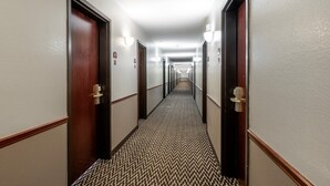 Corredor de hotel com portas, luminárias e carpete estampado.
