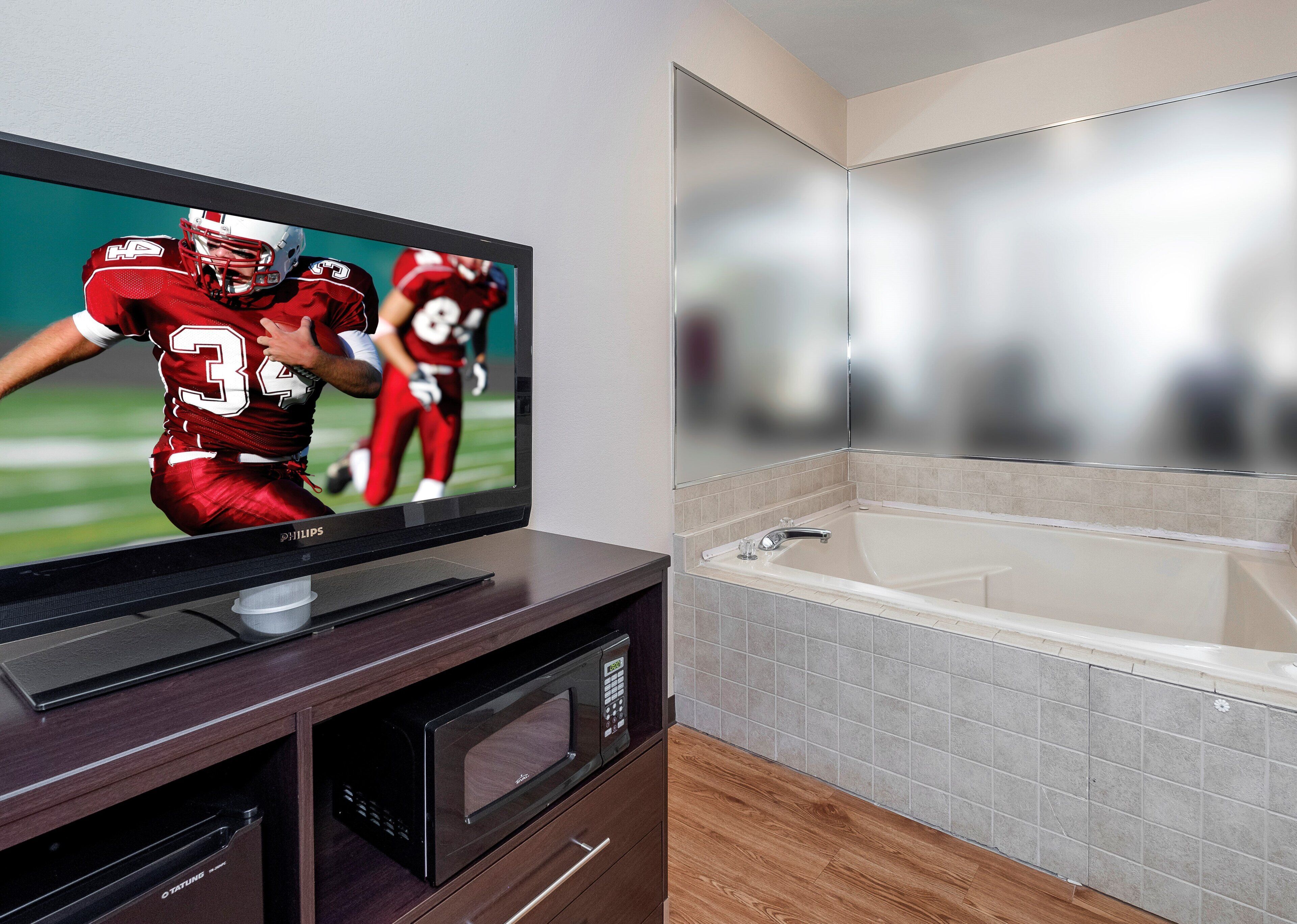 A flat-screen TV on a wooden entertainment unit, a modern bathroom with a bathtub, and a tiled floor.