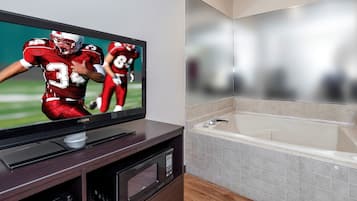A flat-screen TV on a wooden entertainment unit, a modern bathroom with a bathtub, and a tiled floor.