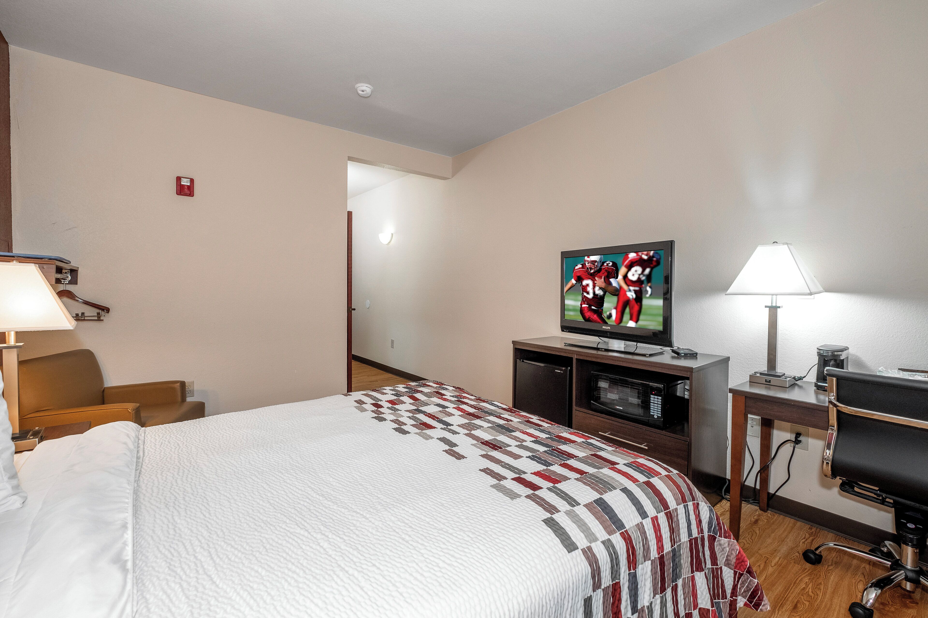 A hotel room with a bed, a television, a desk with a lamp, and a microwave.