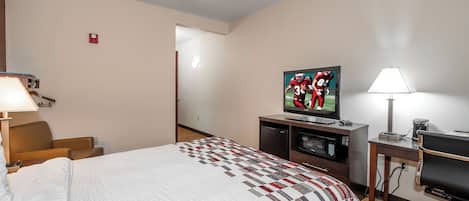 Una habitación de hotel con cama, televisión, escritorio con lámpara y microondas.