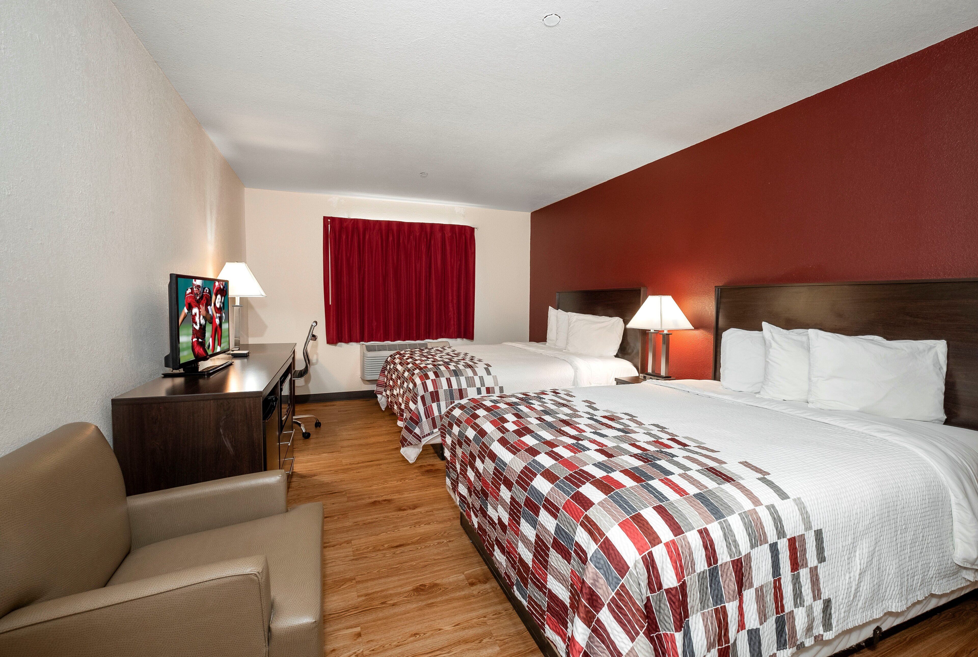A hotel room with two beds, a desk with a computer, a chair, and a TV.