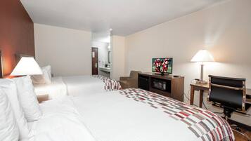 Quarto de hotel com duas camas, televisão, secretária com computador e uma luminária.