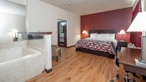 A hotel room with a bed, bedside lamps, a desk, a chair, a mirror, and a bathroom with a bathtub and toilet. - Red Roof Inn Hartselle (Hartselle)
