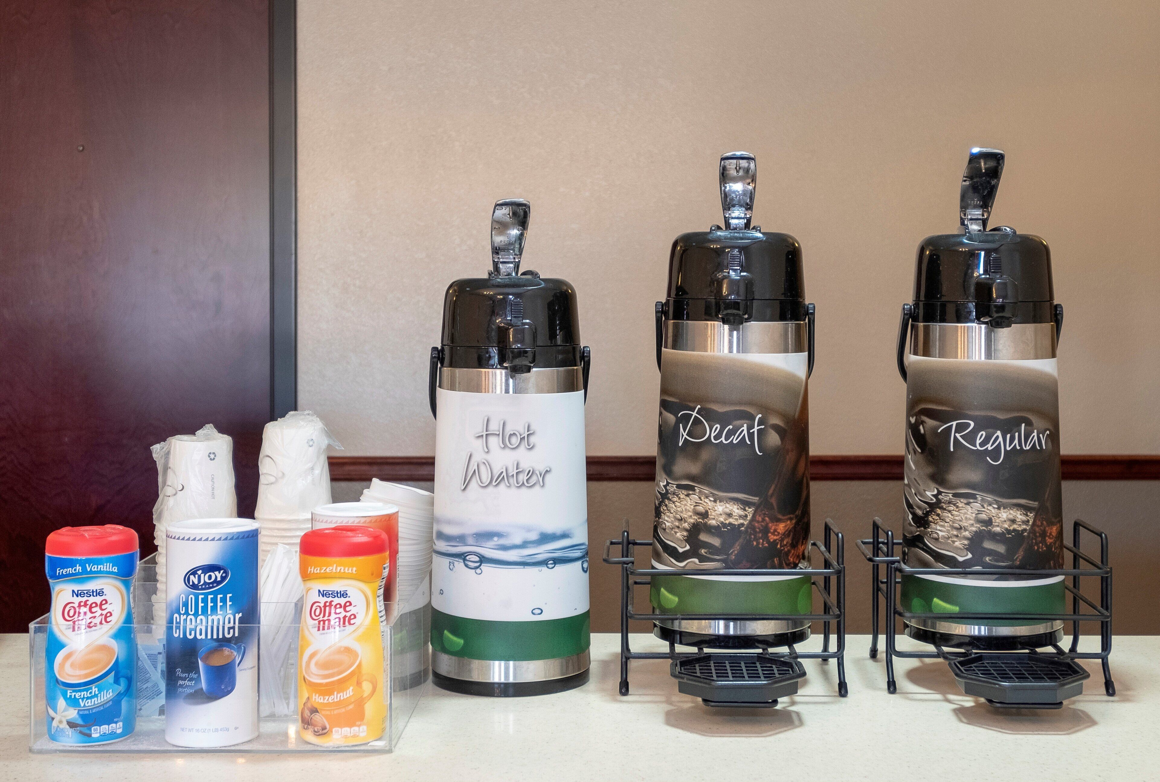 Two coffee makers on a countertop with various coffee creamer options.