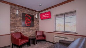 A Red Roof Inn lounge with a stone wall, two red chairs, a small table, a sofa, and a sign indicating free Wi-Fi in all rooms. - Red Roof Inn Hartselle (Hartselle)
