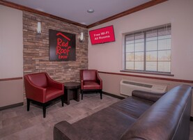 Un salón de Red Roof Inn con una pared de piedra, dos sillones rojos, una mesita, un sofá y un cartel que indica Wi-Fi gratuito en todas las habitaciones.