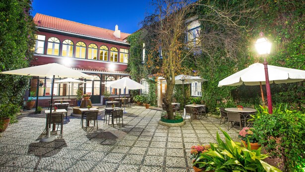 An outdoor patio with tables and chairs, surrounded by potted plants and a building with arched windows. - York House (Lisbon)