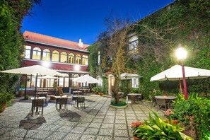 An outdoor patio with tables and chairs, surrounded by potted plants and a building with arched windows. - York House (Lisbon)