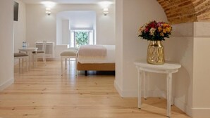 A hotel room with a wooden floor, a bed with a white headboard, a small table with a vase of flowers, and a window with a view of greenery. - York House (Lisbon)
