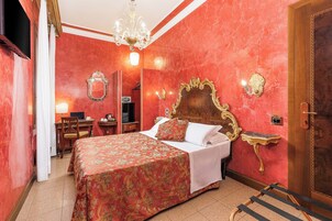 Quarto de hotel com uma cama grande, escrivaninha, cadeira, televisão e lustre.