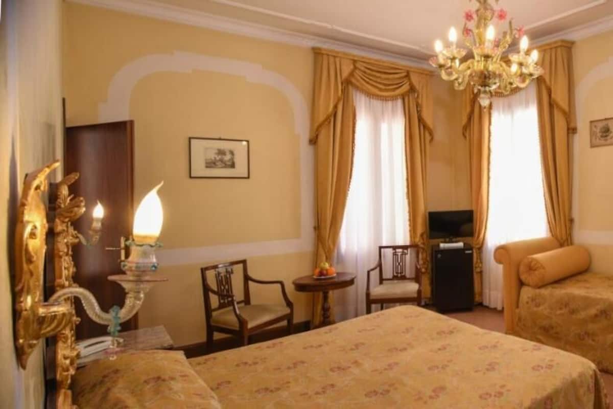 A hotel room with a bed, a sofa, a desk, and a chandelier.