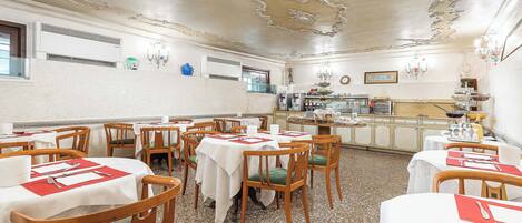 Un comedor con mesas redondas, sillas y una cocina al fondo.