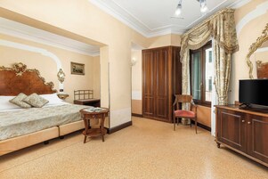 A bedroom with a bed, a wooden wardrobe, a television, and a chair.