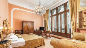 A hotel room with a large bed, a sitting area with a sofa and chairs, a television, and a large window with curtains. - Hotel San Moisè (Venice)