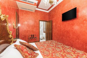 A hotel room with a large bed, a TV mounted on the wall, a wooden chair, and a mirror with an ornate frame.